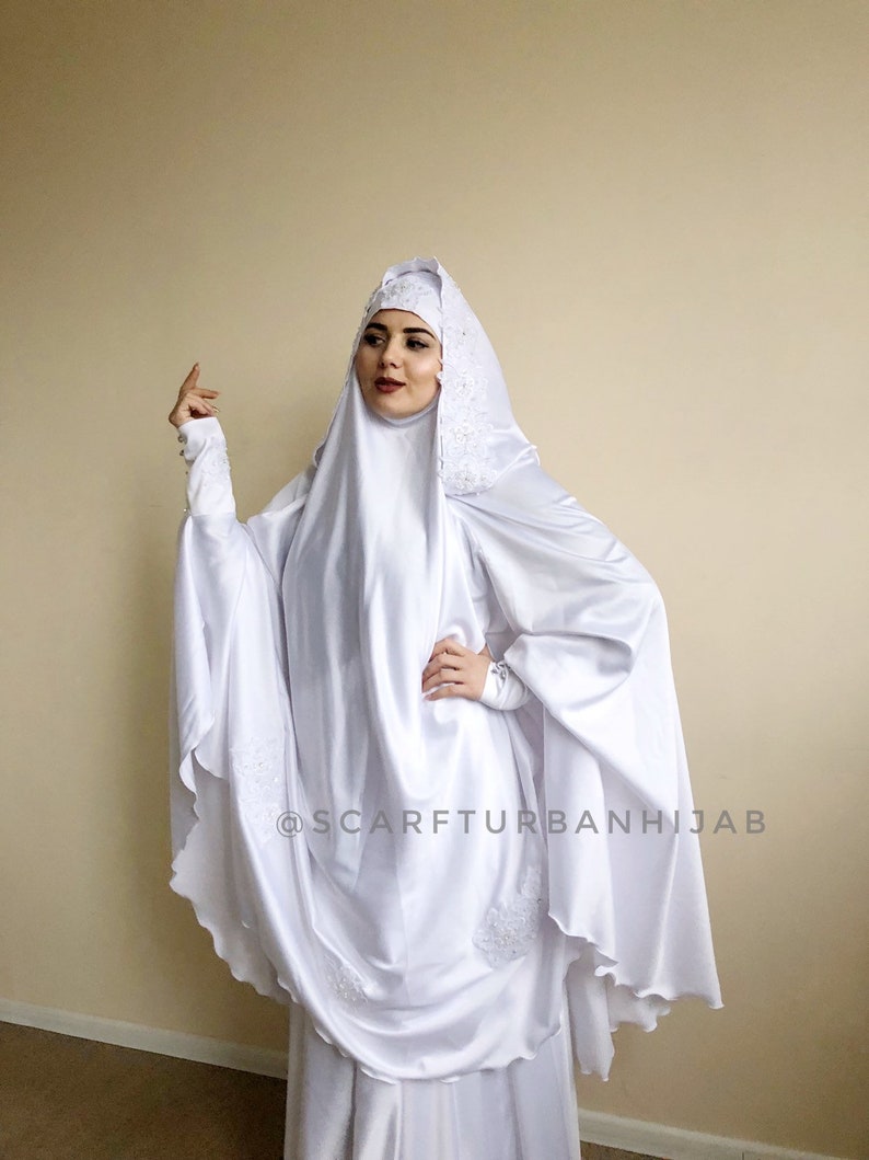 May include: White satin hijab with lace trim and a scalloped edge. The hijab is worn over a white underscarf. The text "@scarfturbanhijab" is visible in the lower right corner of the image.