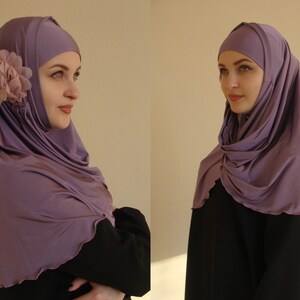 May include: A purple hijab with a flower accent. The hijab is made of a soft, stretchy fabric and is designed to be worn comfortably.