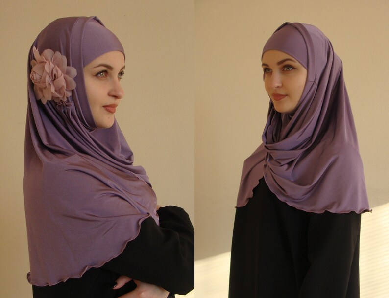 May include: A purple hijab with a flower accent. The hijab is made of a soft, stretchy fabric and is designed to be worn comfortably.