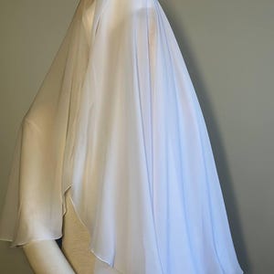 Op de afbeelding: Een witte, doorschijnende sluier gedrapeerd over een mannequin. De sluier is gemaakt van een lichtgewicht stof en heeft een vloeiende, etherische uitstraling.