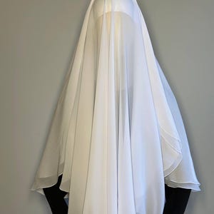 May include: White sheer fabric draped over a mannequin's head, creating a flowing, ethereal look. The fabric is lightweight and translucent, with a soft, delicate texture.
