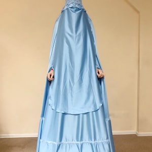 May include: A light blue abaya with a lace trim around the face opening and a ruffled hem. The abaya is made of a silky fabric. The text "@scarfturbanhijab" is visible at the bottom of the image.
