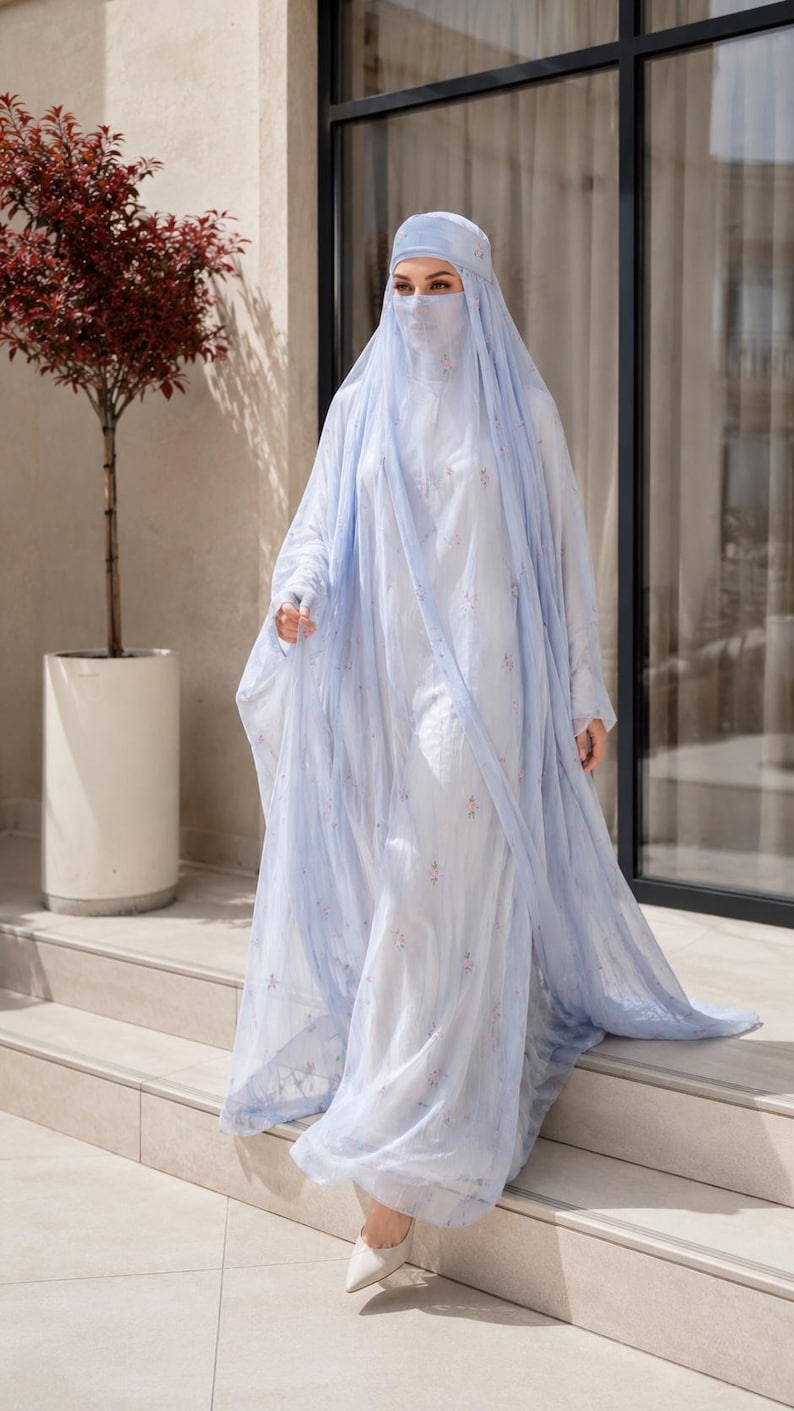 May include: A light blue abaya set featuring a long, flowing outer layer with delicate floral embroidery, paired with a matching head covering and a face veil. The ensemble is crafted from a sheer, lightweight fabric that drapes elegantly.