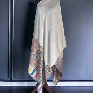 May include: A beige shawl with a colorful paisley border. The border features a variety of colors, including red, blue, green, and yellow.