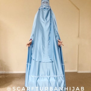 May include: A light blue hijab with a lace trim and a matching headscarf. The hijab is long and flowing, with a gathered skirt. The text "@scarfturbanhijab" is visible at the bottom of the image.