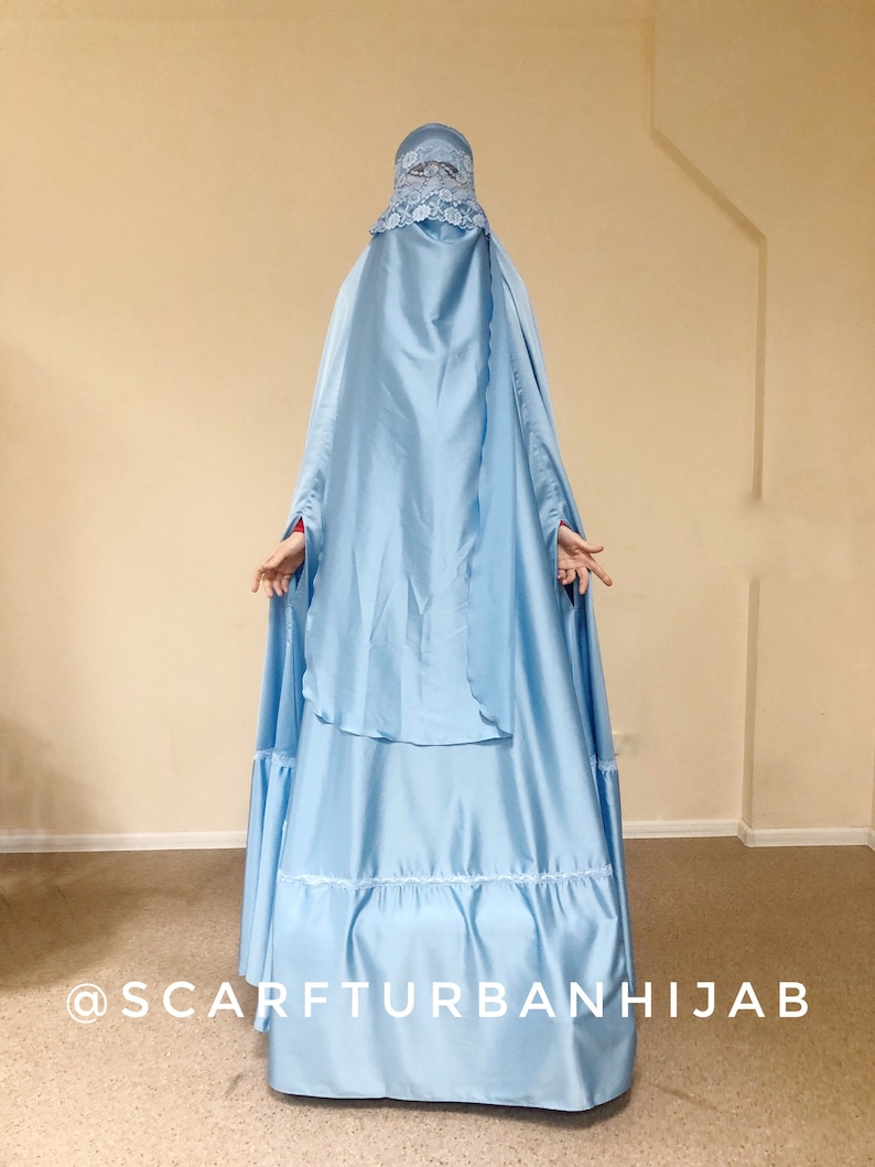 May include: A light blue hijab with a lace trim and a matching headscarf. The hijab is long and flowing, with a gathered skirt. The text "@scarfturbanhijab" is visible at the bottom of the image.