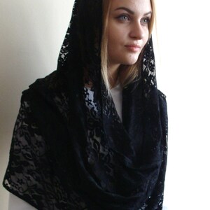 May include: Black lace shawl with a floral pattern. The shawl is draped over a person's head and shoulders.