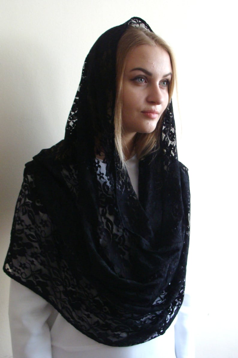 May include: Black lace shawl with a floral pattern. The shawl is draped over a person's head and shoulders.
