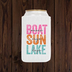 May include: White can cooler with the words "BOAT waves SUN rays LAKE days" in pink, orange, and teal lettering. The top rim is gold. The background is a dark brown wood.