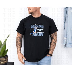 May include: Black t-shirt with the text "Dashing Through The Snow" in white and blue. The graphic features a football player in action. The shirt is a crew neck style.