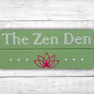 May include: A green wooden sign with the text "The Zen Den" in white lettering. A red lotus flower is centered below the text.
