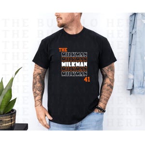 May include: Black t-shirt with a white graphic that says "THE MILKMAN" repeated four times with the number "41" underneath.