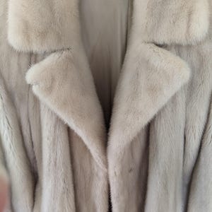 May include: A light beige fur coat with a large collar and a button closure.