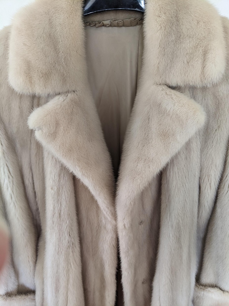 May include: A light beige fur coat with a large collar and a button closure.
