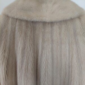May include: A light beige fur coat with a large collar. The fur is soft and fluffy.