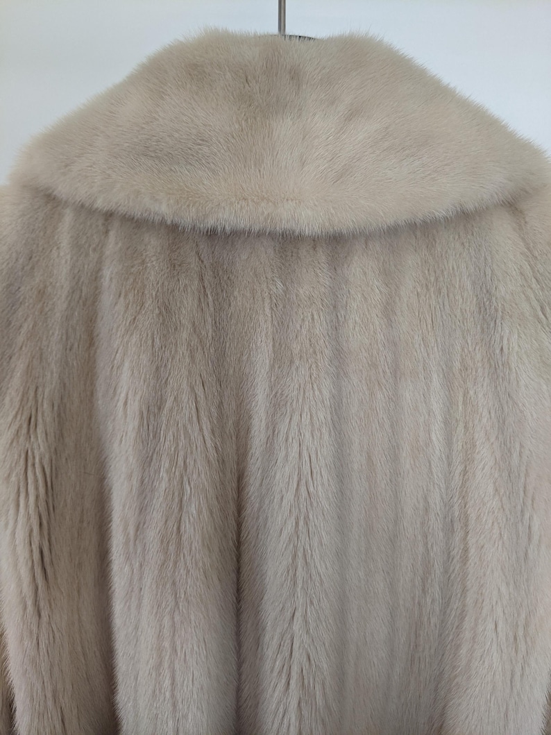 May include: A light beige fur coat with a large collar. The fur is soft and fluffy.