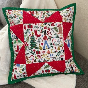 May include: A red and green Christmas pillow with a star design. The pillow is made of fabric with a white background and a variety of Christmas-themed patterns, including a Christmas tree, a nutcracker, and candy canes. The pillow has a green border.