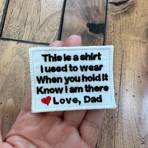 May include: White fabric patch with black embroidered text that reads "This is a shirt I used to wear When you hold it Know I am there Love, Dad" with a small red embroidered heart.