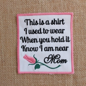 May include: Embroidered patch with the text "This is a shirt I used to wear When you hold it Know I am near Mom." The patch has a pink border and a pink rose with green leaves. The background is a tan burlap.