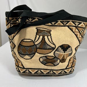 May include: A beige tote bag with black straps and a woven design featuring brown, black, and gray stylized pottery.