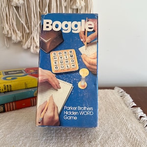 May include: A blue box game called "Boggle" by Parker Brothers. The box features a picture of a game board with letter tiles, a notepad, a pencil, and an hourglass. The text on the box reads "Parker Brothers Hidden Word Game".