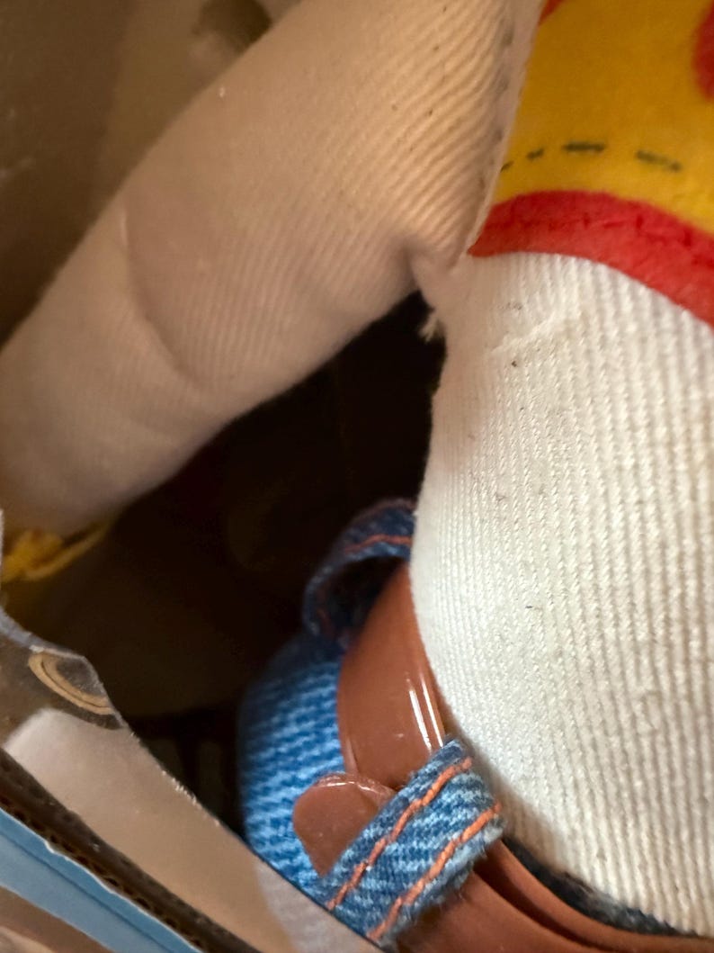 Puede incluir: Primer plano de una mu&ntilde;eca con una corona amarilla y roja, una camisa blanca y zapatos vaqueros azules con suelas marrones. Se ve el brazo de la mu&ntilde;eca, hecho de tela beige. La mu&ntilde;eca est&aacute; dentro de una caja de cart&oacute;n.