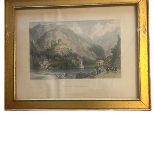 May include: A framed print of a landscape scene with a river, mountains, and a castle in the distance. The print is in a gold frame.