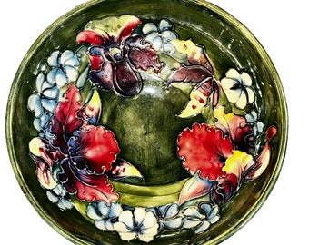 Puede incluir: Un cuenco de cerámica verde con un diseño floral. El cuenco presenta flores rojas, amarillas y moradas con hojas verdes. El cuenco es perfecto para servir aperitivos o postres.