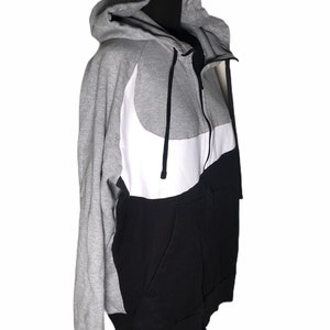 Pode incluir: Um moletom cinza, preto e branco com z&iacute;per e um grande logotipo Nike swoosh branco na frente.