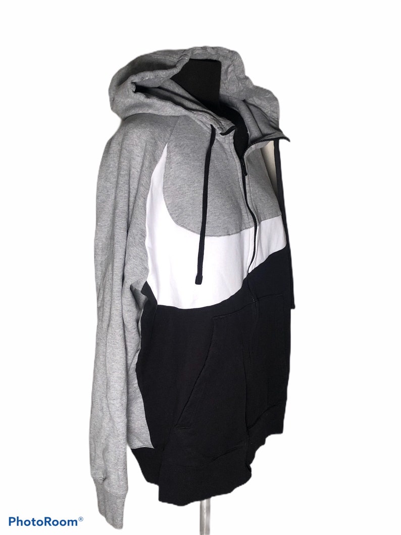 Pode incluir: Um moletom cinza, preto e branco com z&iacute;per e um grande logotipo Nike swoosh branco na frente.