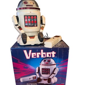 May include: A vintage Verbot robot toy in a white and black color scheme, with a red grid of buttons on its chest. The robot is sitting on top of its original box, which features the Verbot logo and an illustration of the robot. A remote control is also included.