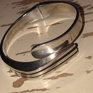 May include: A silver bangle bracelet with a unique, abstract design. The bracelet is made of a smooth, polished metal and has a simple, modern look.