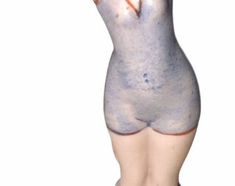 May include: A porcelain figurine of a woman in a blue swimsuit with a red hat. She is standing on a base with a stack of rings.
