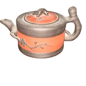 May include: A small, red and black teapot with a floral design. The teapot has a lid and a handle.