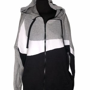 Pode incluir: Um moletom cinza, branco e preto com z&iacute;per e capuz.