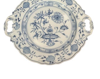 Pode incluir: Um prato de porcelana branca com desenhos florais azuis e duas alças. O prato tem uma borda festonada e uma borda elevada.