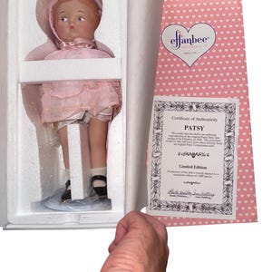 May include: A vintage Patsy doll in a box, wearing a pink dress, hat, and shoes. The doll has a Certificate of Authenticity from Effanbee. The box is white, and the certificate is pink with white hearts. The doll is a limited edition.