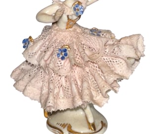 May include: A porcelain figurine of a ballerina wearing a pink lace dress with blue flowers. The ballerina is posed in a twirling motion with her right arm extended.