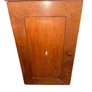 May include: A vintage wooden cabinet with a single door. The cabinet is made of dark wood with a natural finish. The door has a simple design with a single panel and a small metal knob.