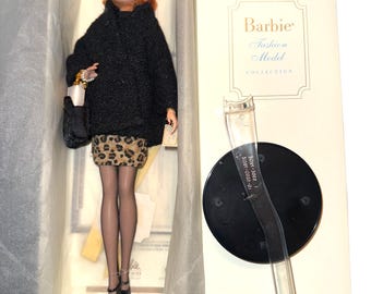 May include: A Barbie Fashion Model doll in a box. The doll has red hair, glasses, and a black coat over a leopard print skirt. The box reads "FAO Schwarz Limited Edition" and "Barbie Fashion Model Collection."