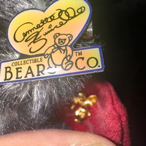 May include: A collectible bear tag with a heart-shaped design, featuring the text "Comesse Zunice" and a bear illustration. The tag also includes the text "COLLECTIBLE BEAR CO."