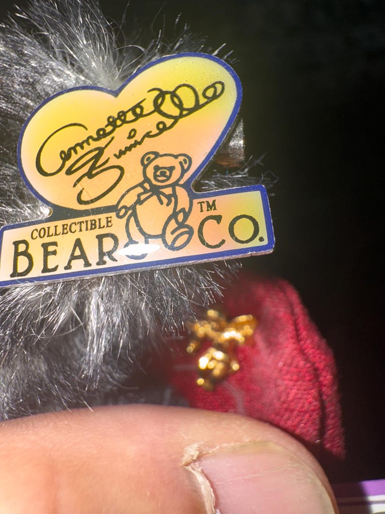 May include: A collectible bear tag with a heart-shaped design, featuring the text "Comesse Zunice" and a bear illustration. The tag also includes the text "COLLECTIBLE BEAR CO."