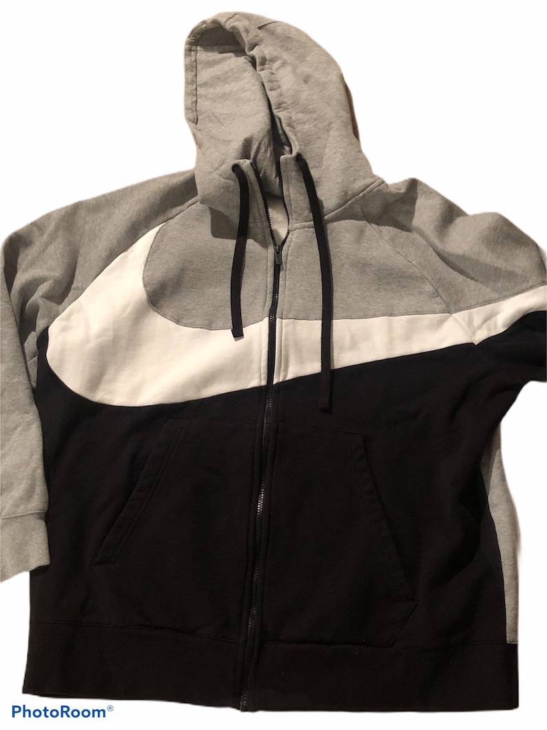 Pode incluir: Uma jaqueta com capuz cinza, branca e preta com z&iacute;per e um grande logotipo Nike swoosh.