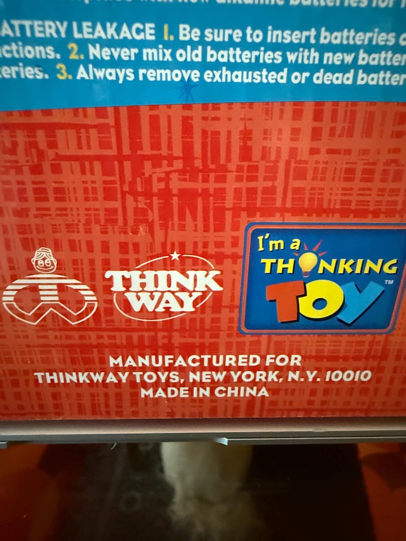 Puede incluir: Primer plano de una caja roja y blanca con el logotipo de Think Way Toys y el texto "I'm a THONKING TOY". La caja tambi&eacute;n incluye instrucciones sobre fugas de bater&iacute;a y el texto "MADE IN CHINA".