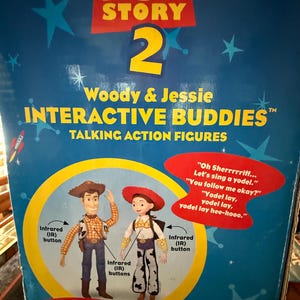 Puede incluir: Caja azul de Toy Story 2 con figuras de acci&oacute;n parlantes Woody y Jessie Interactive Buddies. La caja tiene gr&aacute;ficos de estrellas y cohetes. Woody lleva sombrero de vaquero, chaleco y vaqueros. Jessie lleva sombrero rojo y pantalones con estampado de vaca.