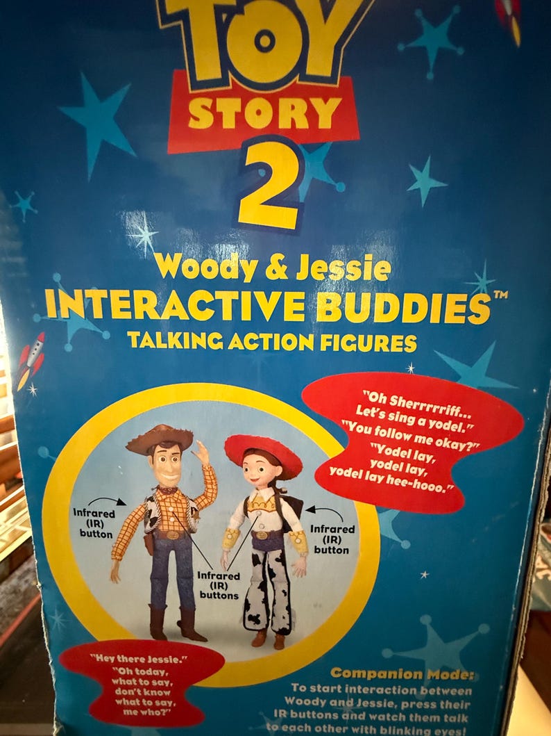 Puede incluir: Caja azul de Toy Story 2 con figuras de acci&oacute;n parlantes Woody y Jessie Interactive Buddies. La caja tiene gr&aacute;ficos de estrellas y cohetes. Woody lleva sombrero de vaquero, chaleco y vaqueros. Jessie lleva sombrero rojo y pantalones con estampado de vaca.