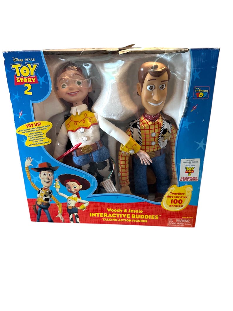Puede incluir: Un juego de figuras de acci&oacute;n parlantes interactivas de Woody y Jessie de Toy Story 2 de Disney Pixar. La caja presenta im&aacute;genes de los personajes y el texto "Woody & Jessie INTERACTIVE BUDDIES". La caja es azul y blanca.