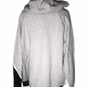 Pode incluir: Uma camisa de moletom cinza com capuz com detalhes em preto e branco. A camisa de moletom tem uma faixa preta na parte inferior e mangas pretas com detalhes em branco.