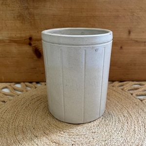 May include: White ceramic utensil holder with vertical lines. The holder is sitting on a woven rug.