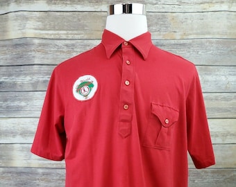 May include: Red short-sleeved polo shirt with a white patch on the left chest that says "World Series" with a baseball and clock graphic.